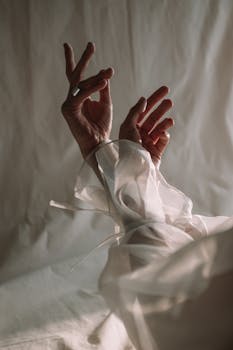 在白色背景下，优雅的双手与丝绸相映，姿态尽显优雅