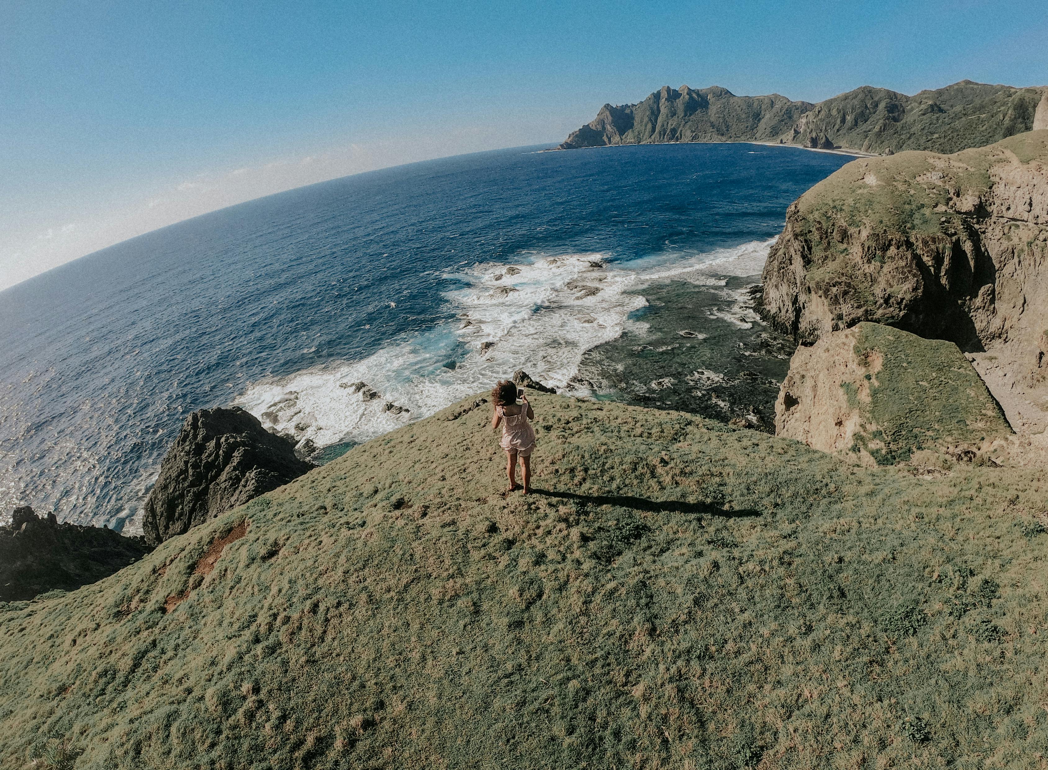 woman in black tank top and blue denim shorts standing on rock formation near body of during