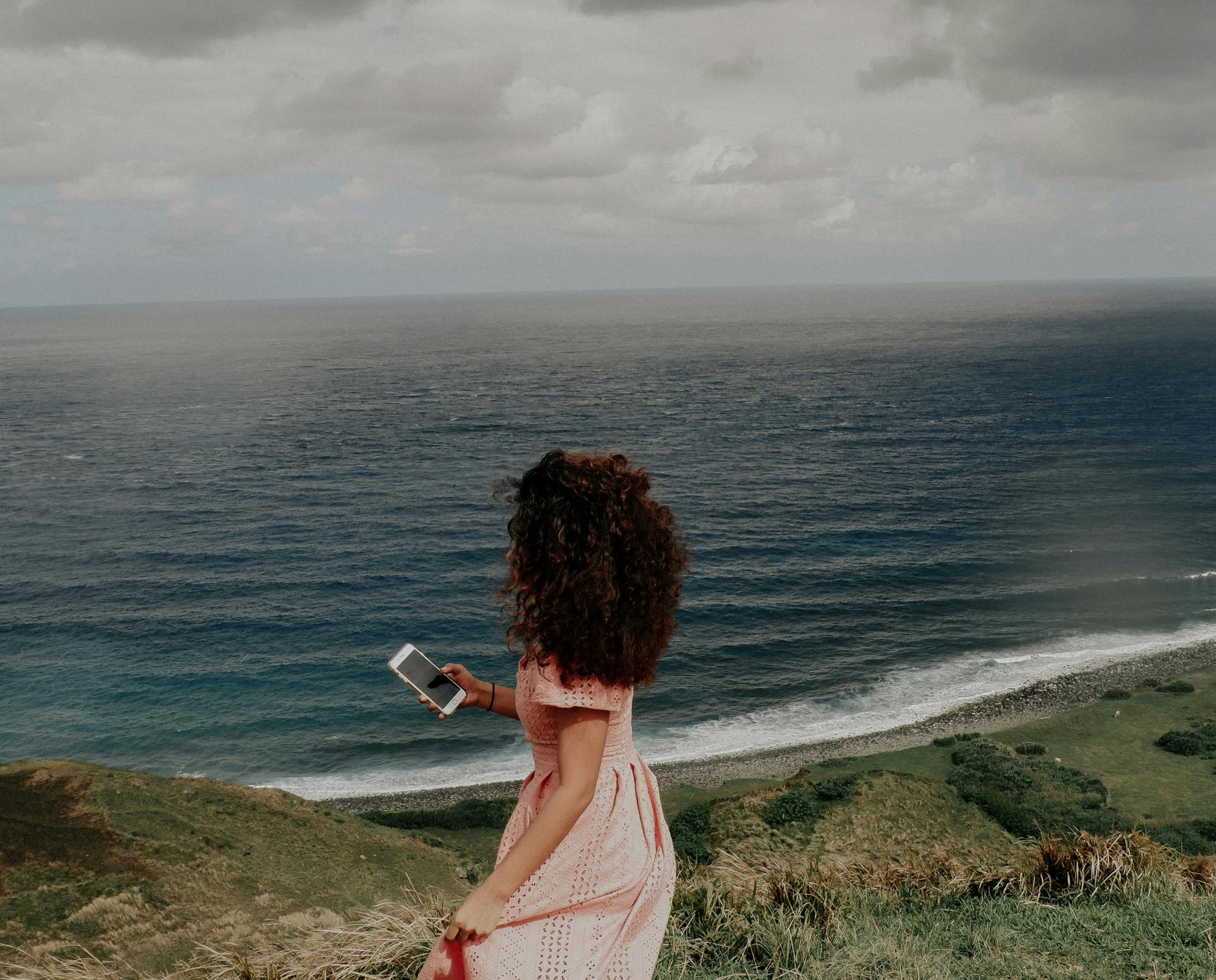 A woman enjoying the scenic coastline of Cagayan Valley, Philippines with a smartphone in hand.