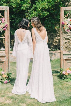 A romantic same-sex wedding with two brides in elegant white gowns holding hands outdoors.