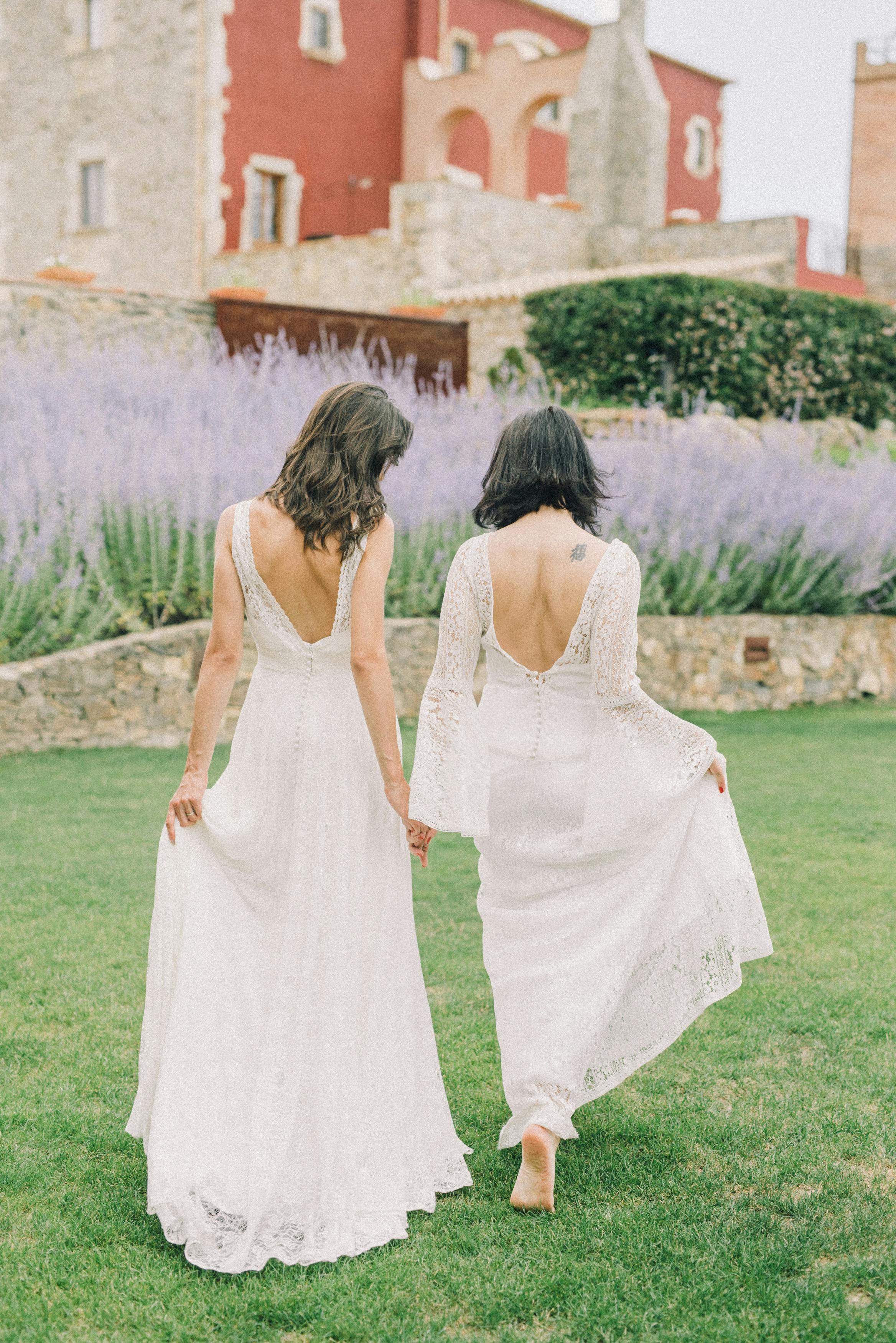 photo of two women in white wedding dress walking on grass field