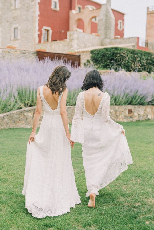 Photo of Two Women in White Wedding Dress Walking on Grass Field