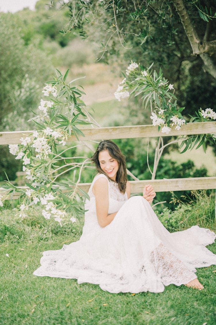 Woman In Wedding Dress Sitting On Grass While Smiling