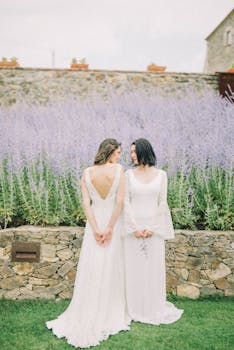 Elegant lesbian couple in bridal gowns during an outdoor wedding ceremony.