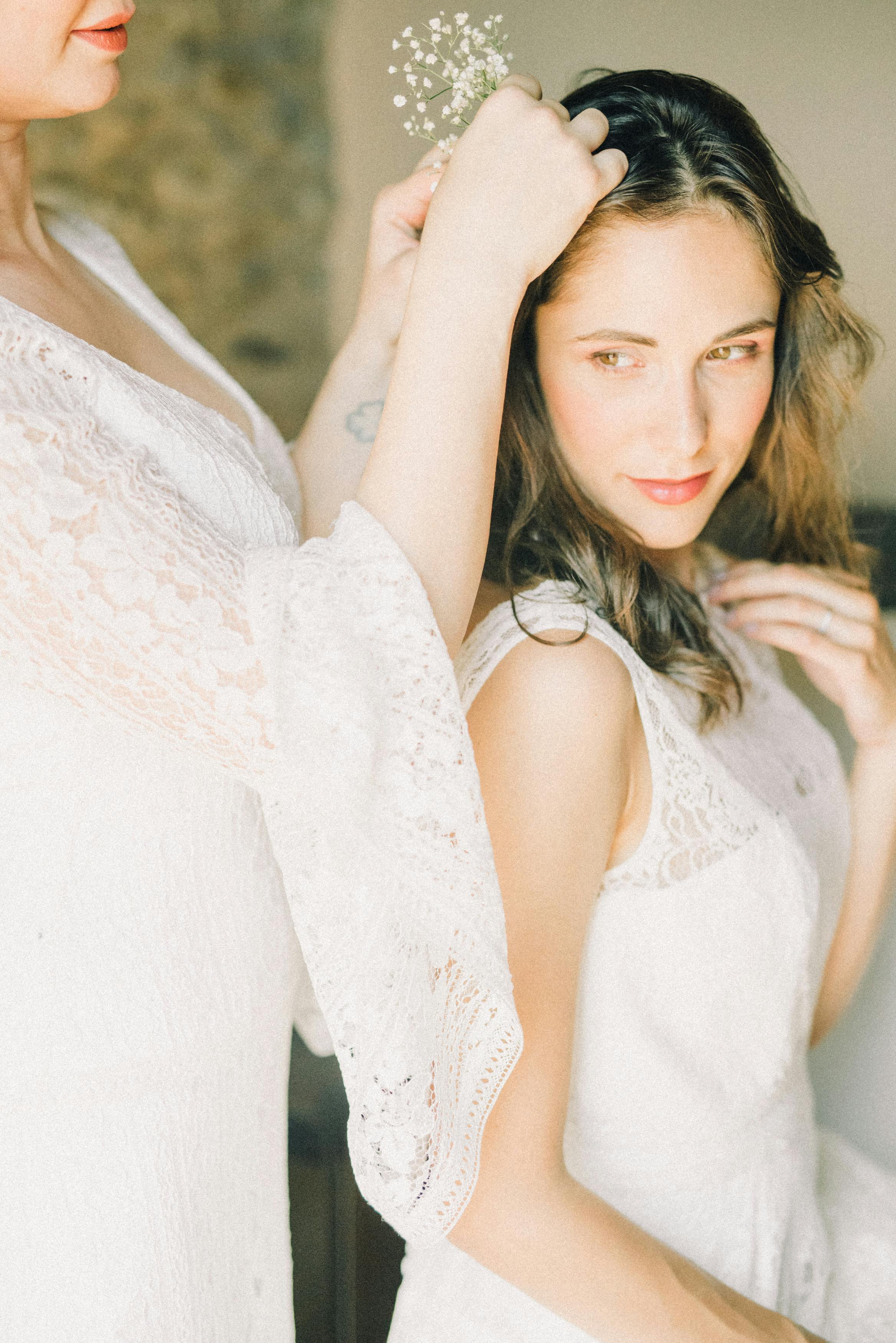 Two brides preparing for their wedding day, delicately arranging flowers in a bright indoor setting.