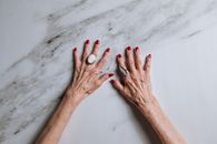一位上了年纪的妇女，双手涂着红指甲、戴着戒指，背景是大理石
