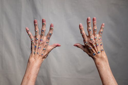 Two elderly hands artfully decorated with flashling rhinestones against a neutral background.