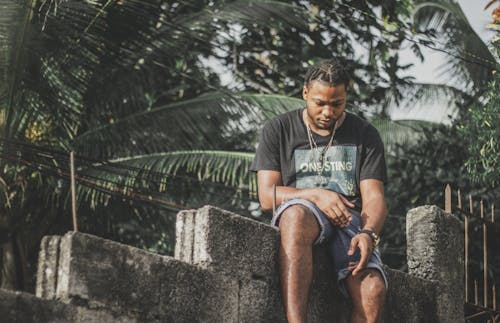 Man in Black Crew Neck T-shirt Sitting on Concrete Blocks