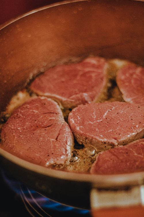 Free A detailed shot of raw beef slices sizzling in a copper frying pan, ready for cooking. Stock Photo