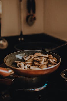 Delicious sliced mushrooms being sautéed in a frying pan on a stove.