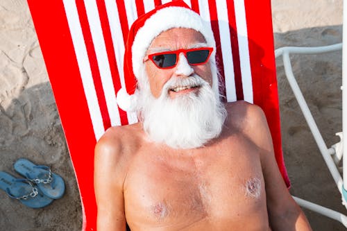 Photo of Man Wearing Santa Hat While Lying on Beach Chair