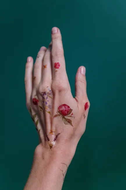 Petits tatouages temporaires floraux en couleur, roses et lavande, sur le dos d'une main, fond vert