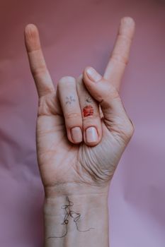 Artistic hand gesture with temporary tattoos on a pink background, symbolizing rock music and self-expression.