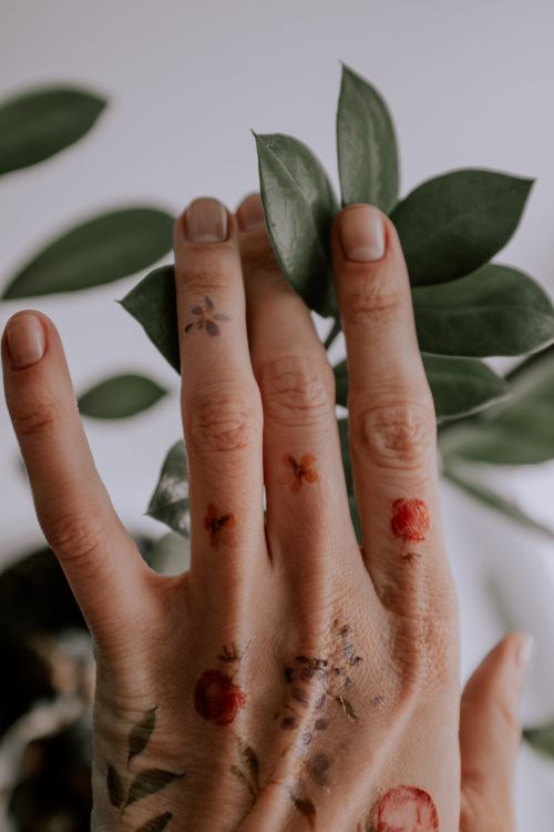 Free Close-up of a tattooed hand touching green leaves, showcasing nature and art. Stock Photo