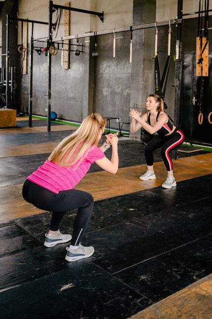 Two women performing squats in a modern gym setting, enhancing fitness and motivation.