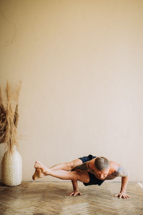 Free An athletic man in shorts performing a complex yoga pose indoors on a wooden floor. Stock Photo