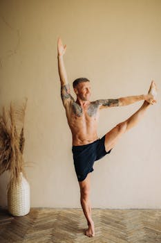 Athletic man practicing yoga indoors with tattoos, promoting wellness and flexibility.