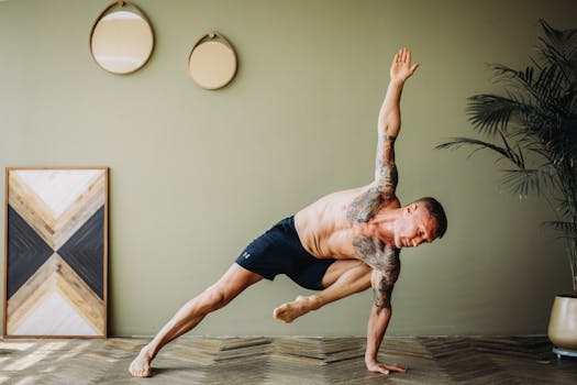 A shirtless man with tattoos performing a yoga pose indoors, showcasing flexibility and strength.