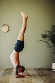 Shirtless man practicing forearm balance yoga pose indoors, promoting wellness and flexibility.