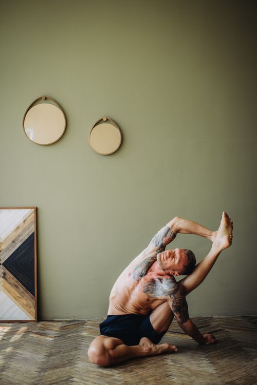 Free Shirtless man with tattoos performing yoga in a minimalist room, showcasing flexibility and wellness. Stock Photo