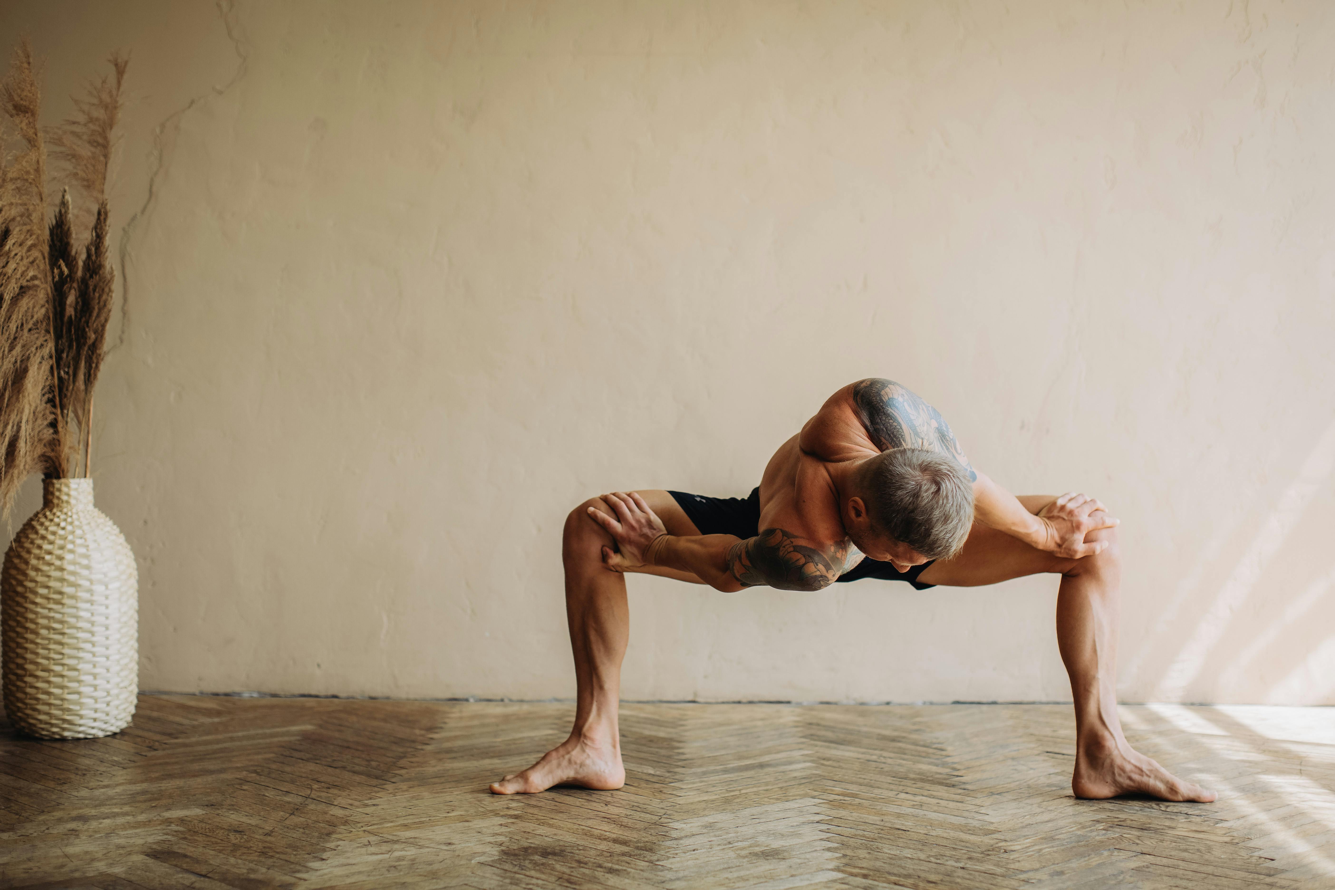 A shirtless man practicing yoga indoors displaying flexibility and muscle definition.