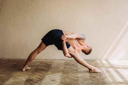 Free Athletic man performing a deep stretching yoga pose indoors with bare feet and tattoos. Stock Photo