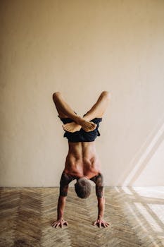 A man executes a challenging handstand yoga pose indoors, showcasing flexibility and strength.