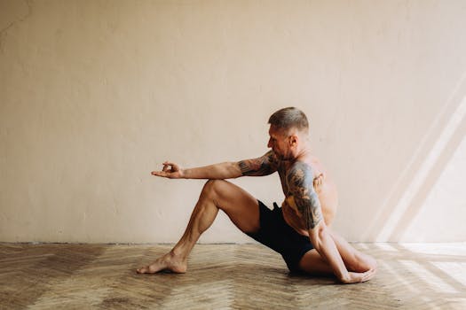 Tattooed man performing yoga indoors, showcasing strength and flexibility in a serene setting.