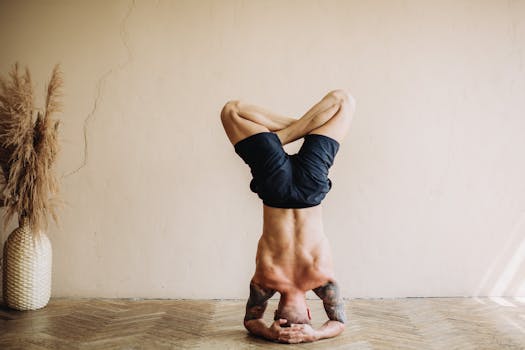 Shirtless man practicing headstand yoga indoors, showcasing strength and flexibility.