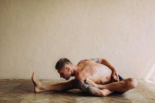 Tattooed man practicing a challenging yoga pose indoors, showcasing flexibility and strength.