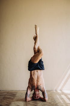 Tattooed male in shorts doing headstand yoga pose indoors showcasing strength and balance.