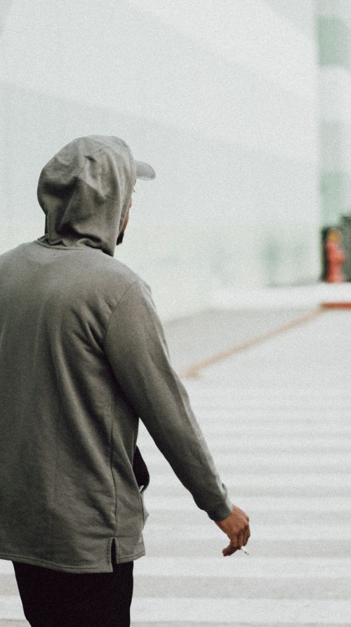 Free Back view of a man in a gray hoodie and cap, casually walking outdoors. Stock Photo