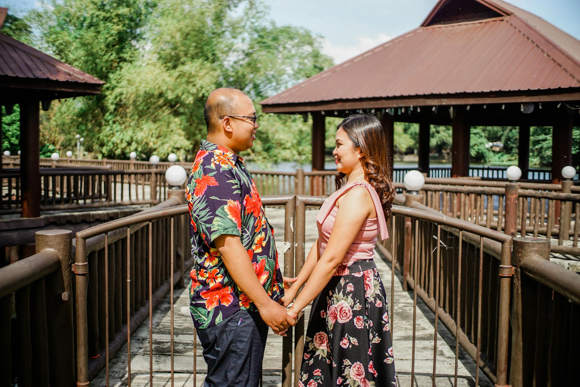 A happy couple holding hands and smiling at each other in an outdoor gazebo setting, expressing love and togetherness.