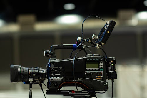 Contemporary professional film camera with wires and display under glowing lights in building