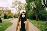 一名女子戴着口罩，站在树木环绕的公园里，说明户外防护的重要性