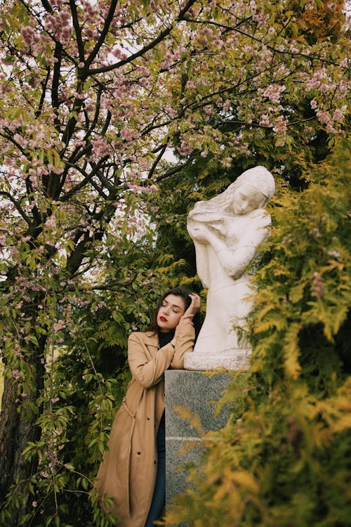 Photo of Woman in Brown Coat Leaning on Statue