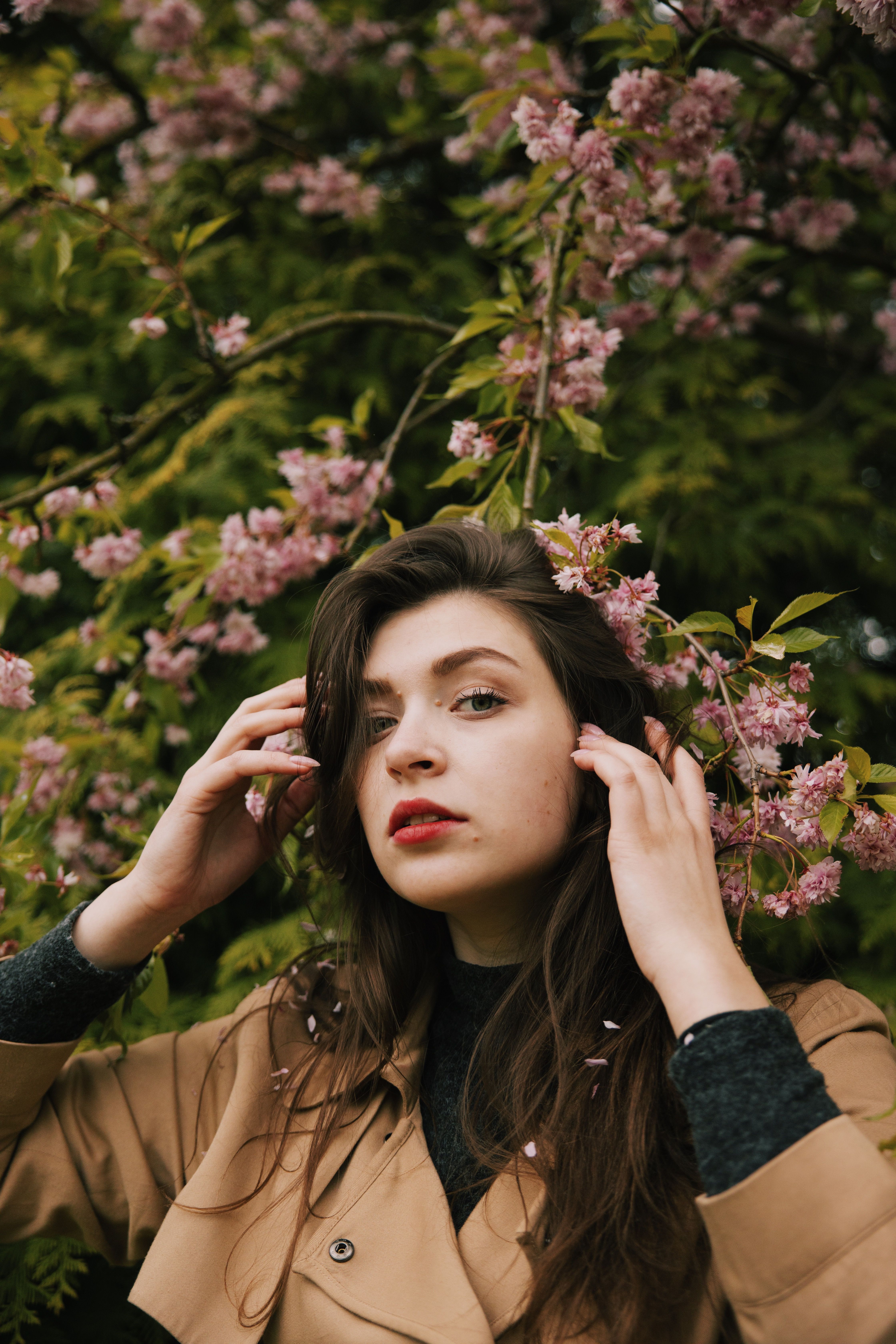 Photo of Woman in Brown Coat Standing Near Pink Flowers · Free Stock Photo