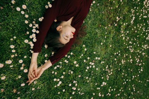 Free Woman lying peacefully on a grassy field with daisies, embodying relaxation and nature connection. Stock Photo