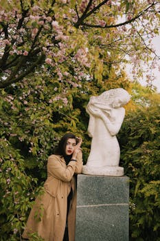 一名女子站在花园里，旁边是一棵盛开的树下的白色大理石雕像