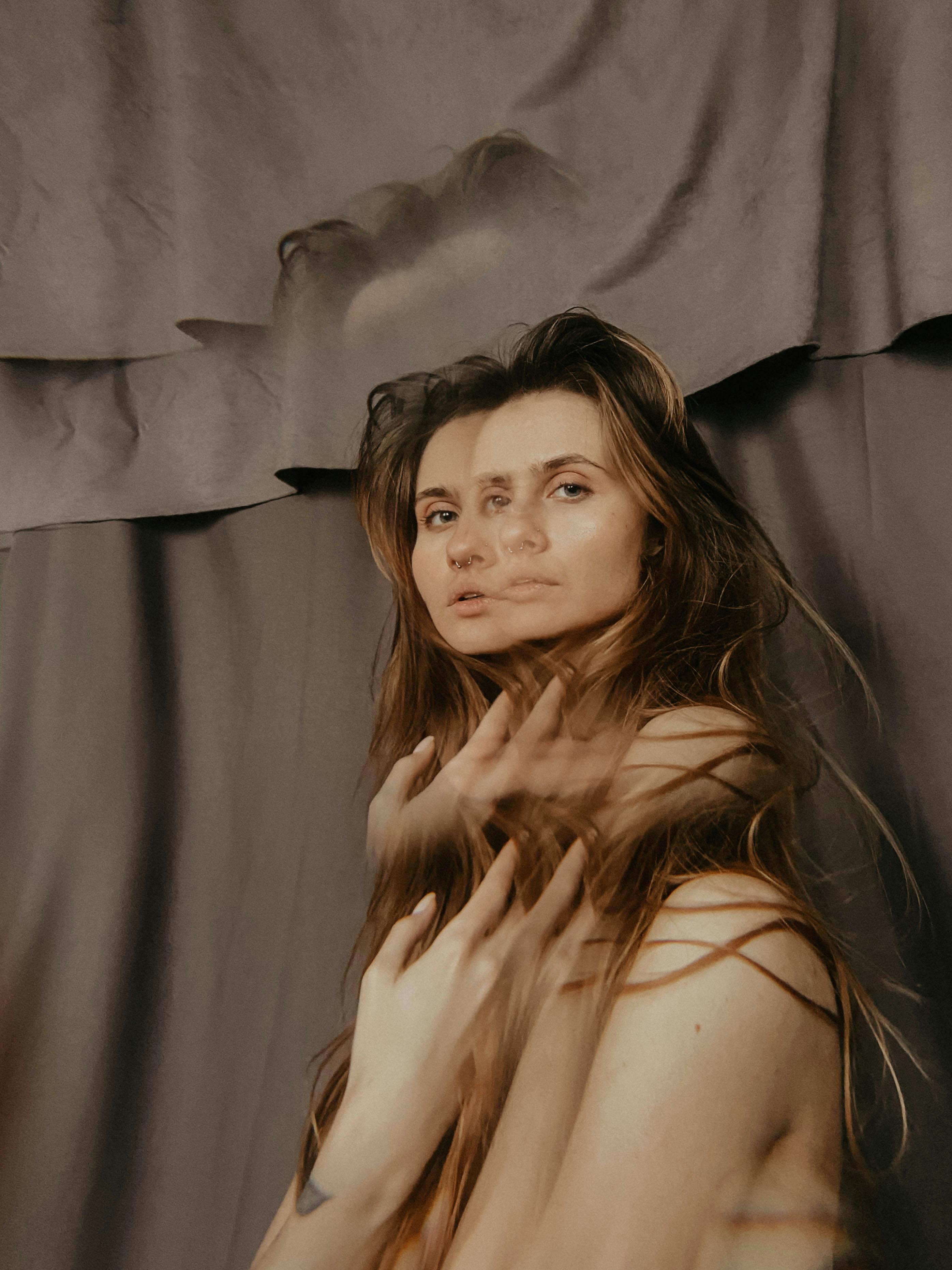 这幅双重曝光肖像富有创意，描绘了一位头发飘逸的女性，她映衬着棕色窗帘，散发着神秘而艺术的氛围