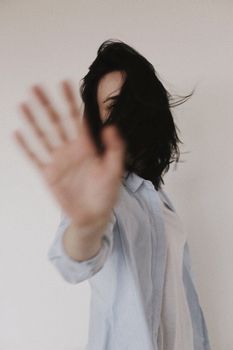 一名黑发女子伸手遮住脸，背景是白色