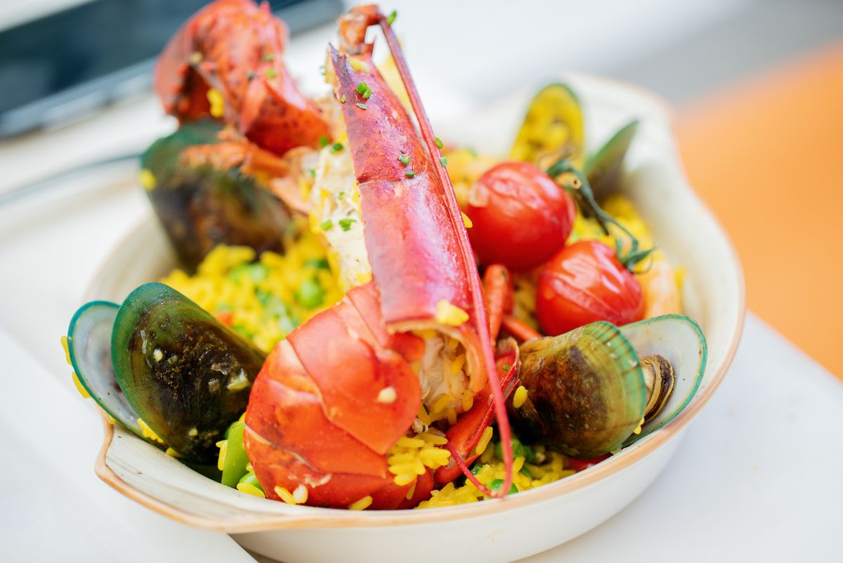 Oval dish of saffron rice with a split lobster tail, claw, green-lipped mussels and cherry tomatoes