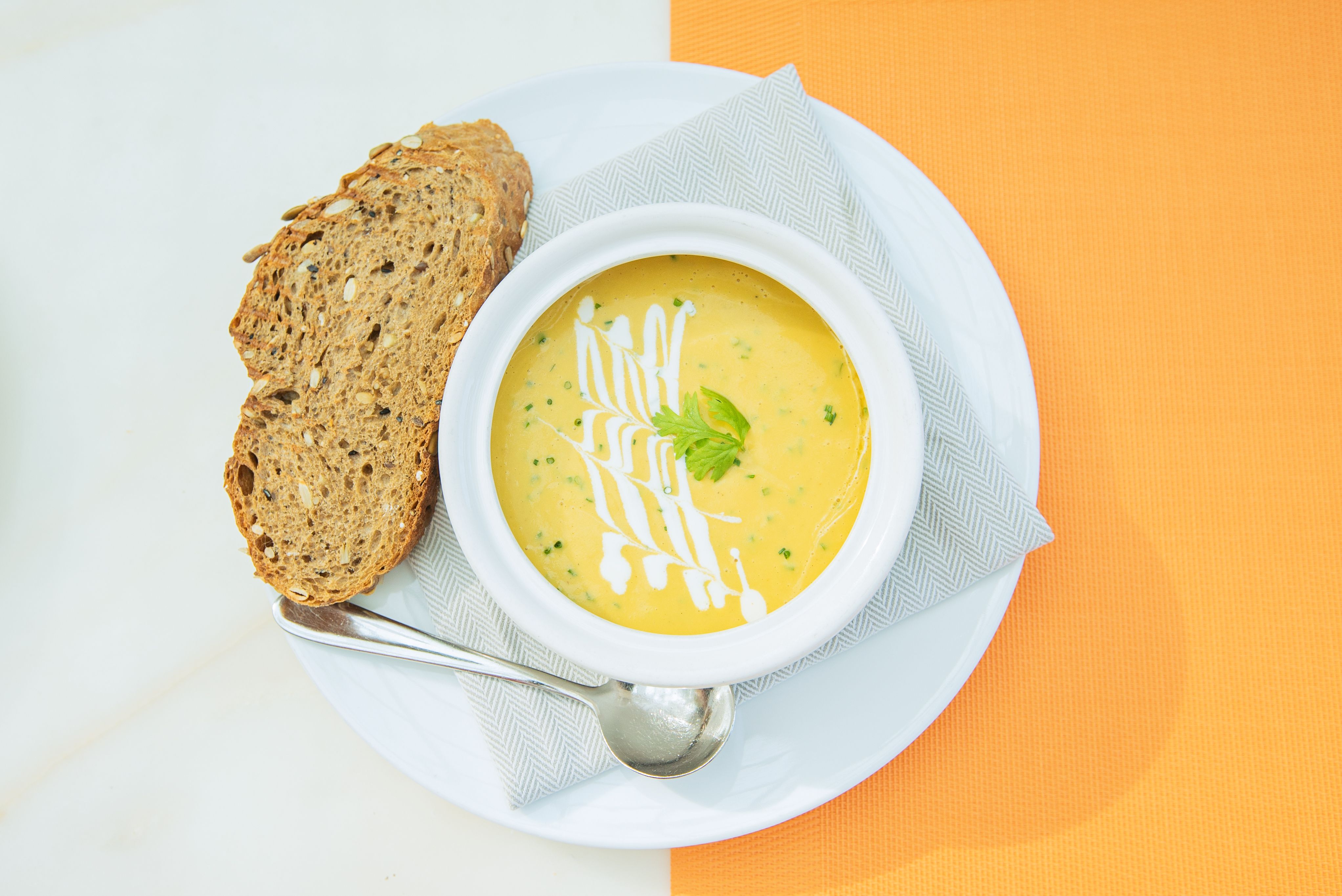 A bowl of creamy vegetable soup garnished with cream and herbs, served with artisan bread.