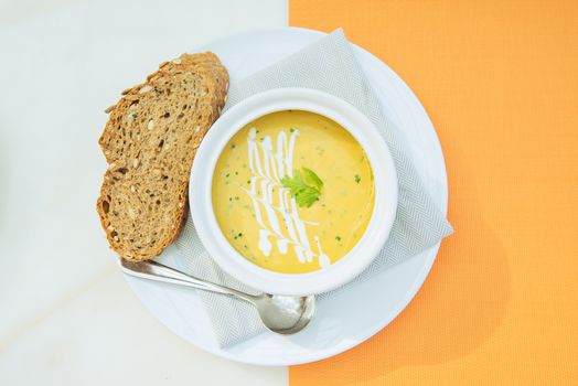 A bowl of creamy vegetable soup garnished with cream and herbs, served with artisan bread.