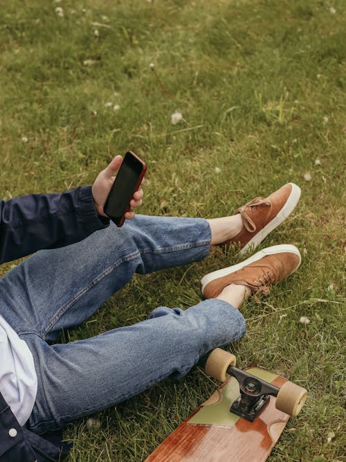 Person in Blue Denim Jeans and Brown Sneakers Sitting on Grass Field