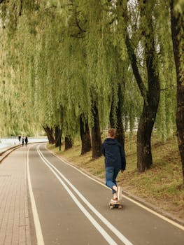 一名年轻的滑板运动员穿着休闲装，沿着绿树成荫的公园小路骑行，享受着户外时光