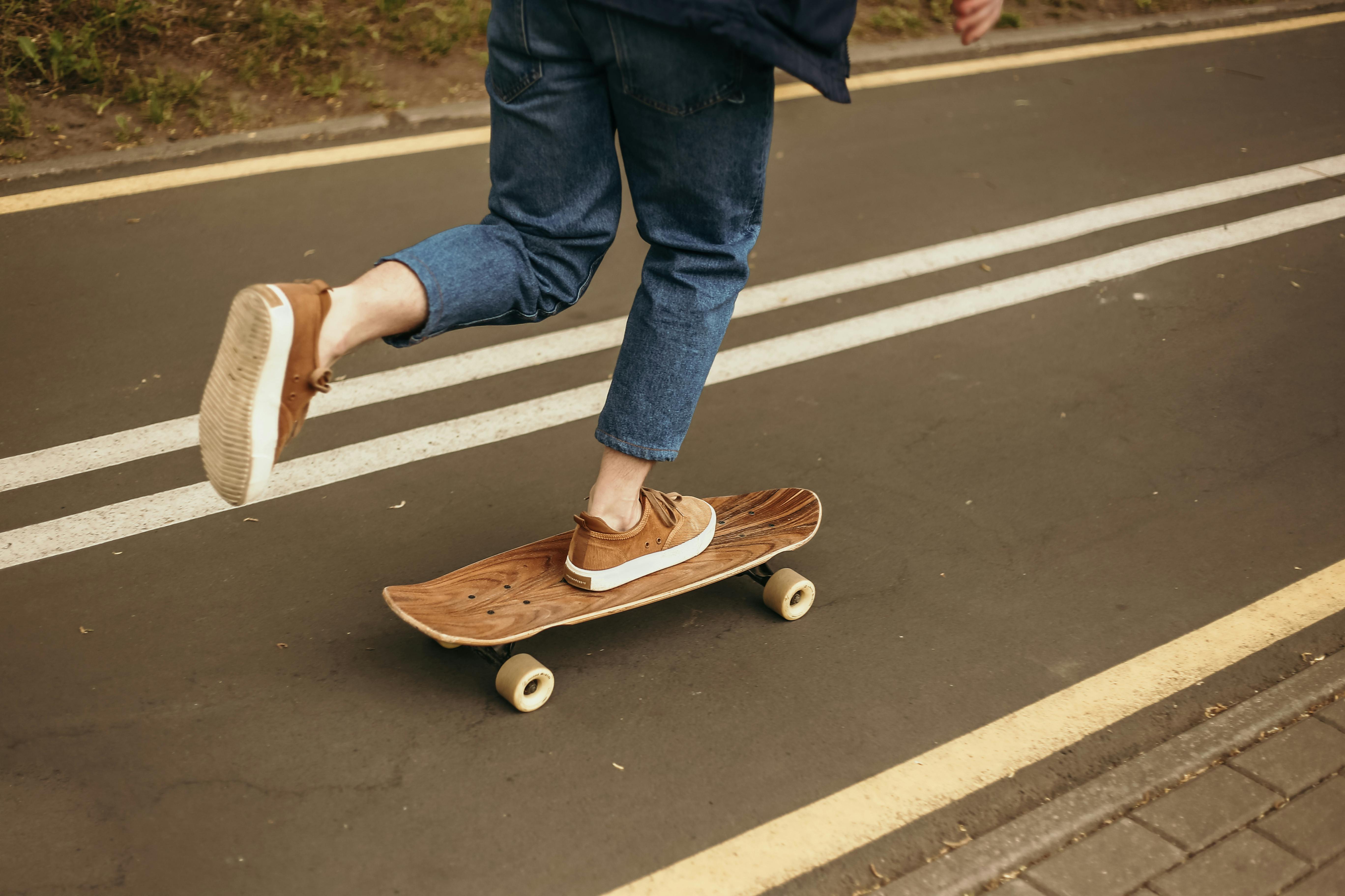 person in blue denim jeans and brown shoes standing on a skateboard on gray concrete road