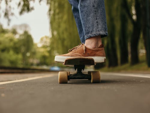 Person in Blue Denim Jeans and Brown Leather Shoes Riding on Skateboard