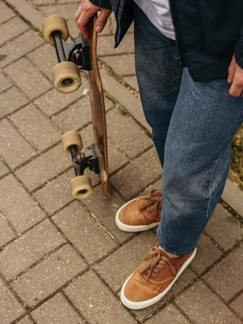 Person in Denim Jeans and Brown Shoes Holding a Longboard