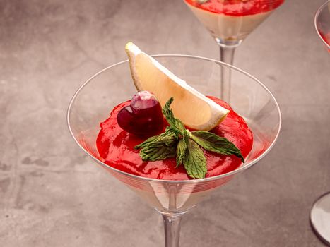 Close-up of a strawberry mousse dessert garnished with mint and lemon slice in a cocktail glass.